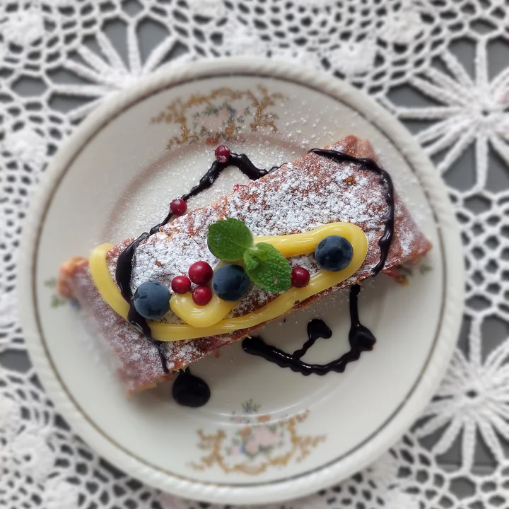 A slice of berry cake with cream, berries and mint on a plate